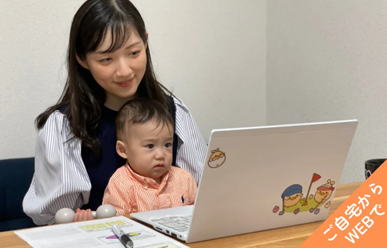 自宅でノートPCに向かうオンライン体験中の母親と赤ちゃん